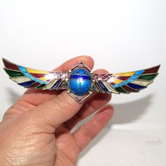 a hand holding a blue and green insect brooch with wings on it's back