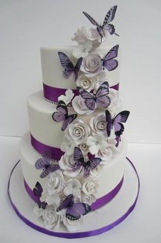 a three tiered cake with purple and white flowers on the top, and butterflies on the side