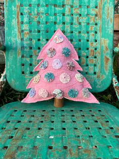 a pink christmas tree sitting on top of an old green chair with buttons and shells