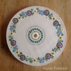 a white plate with blue, yellow and green flowers on it sitting on a wooden table