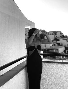 a woman in a long black dress is standing on a balcony looking at the city