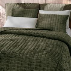 a bed with green bedspread and pillows on top of it, next to a wooden headboard