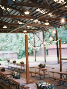 tables and benches are set up in an open area with lights strung from the ceiling