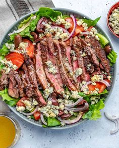 steak salad with tomatoes, onions and feta cheese in a bowl next to a glass of orange juice