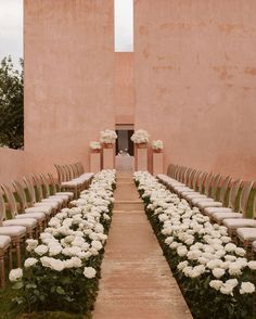 an outdoor ceremony setup with chairs and flowers on the aisle, in front of two large pink walls