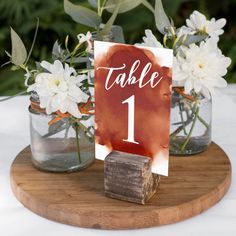 the table numbers are displayed in mason jars with wood block holders holding white flowers and greenery