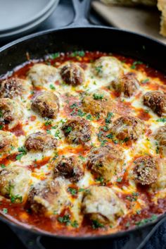 a pan filled with meatballs and sauce on top of a table next to bread