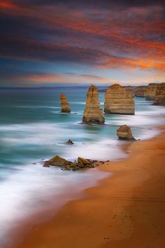 the beach is lined with large rocks under a colorful sky at sunset or sunrise time