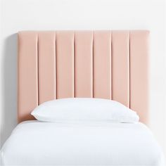 a bed with a pink headboard and pillows on top of it, against a white wall