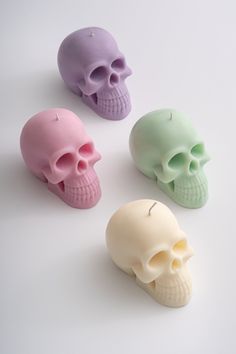 three different colored skulls sitting next to each other on a white surface with one candle in the shape of a skull