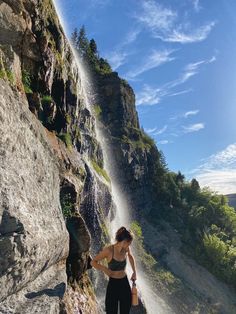 a woman standing on the side of a cliff next to a waterfall with water coming out of it