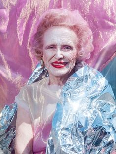 an older woman with white makeup and red lips is wrapped in aluminum foil while sitting on a pink chair