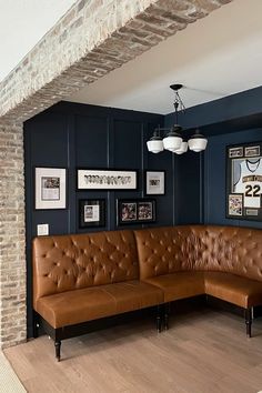 a brown leather couch sitting in front of a brick wall with pictures hanging on it