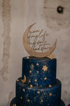 a three tiered blue cake with gold stars and moon decorations on the top layer