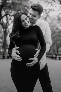 a pregnant couple cuddles in the park for their black and white photo session