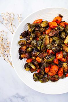 a white bowl filled with brussel sprouts and carrots on top of a marble counter