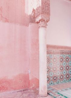 an old column in the corner of a room with pink and blue tiles on it