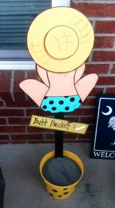 a sign with a hat on it in front of a brick wall and a potted plant