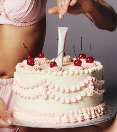 a woman is holding a cake with cherries on it and pointing to the top