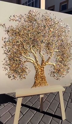 a gold tree is on display in front of a white canvas with silver and gold glitters