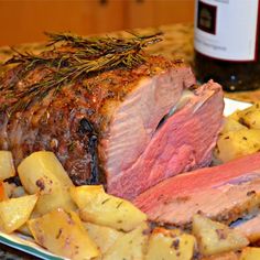 a plate with roast and potatoes on it next to a bottle of wine in the background