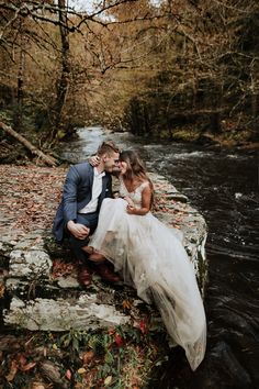 a bride and groom sitting on the edge of a river