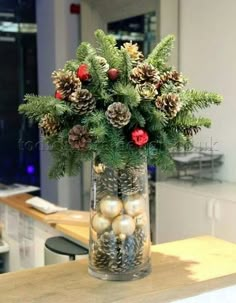 a glass vase filled with pine cones and christmas balls on top of a wooden table