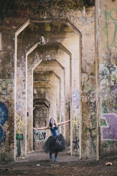 a woman in a black tutu is dancing under an old bridge