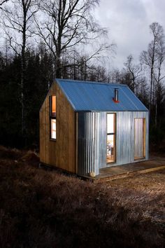 a small metal building sitting on top of a grass covered field in front of trees