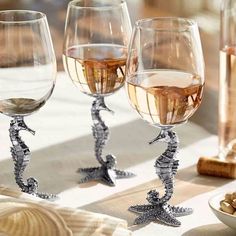 three wine glasses sitting on top of a table with seahorses in the middle