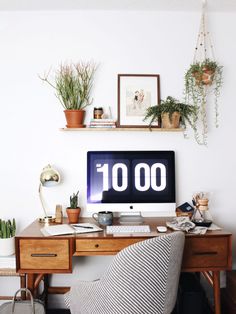 a desk with a computer and plants on it