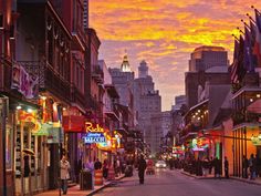 a city street at sunset with people walking on the sidewalk and buildings in the background