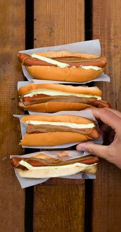 four hotdogs with mustard and ketchup in buns on wooden table