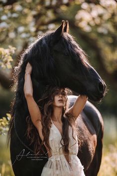 a woman in a white dress standing next to a black horse with her hands on the head