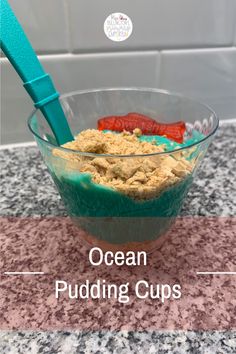 an ocean pudding in a glass bowl with a blue spatula on top and the words ocean pudding cups below it