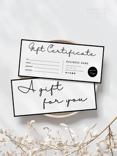 two gift certificates sitting on top of a plate next to some dried flowers and leaves