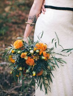 a woman in a white dress holding a bouquet of orange and yellow flowers on her wedding day