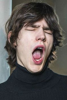 a young man with his mouth open and tongue out in front of him, wearing a black turtle neck sweater