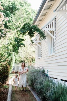 a woman and child walking down a path in front of a house with lavender bushes