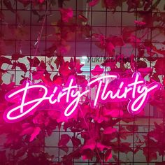 a neon sign that says dirty thirty above some pink leaves on a tiled wall behind it