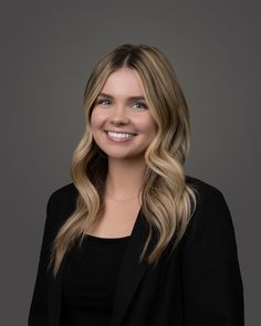 a woman with long blonde hair wearing a black blazer and smiling at the camera