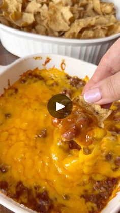 a person dipping some tortilla chips into a casserole dish with cheese and chili