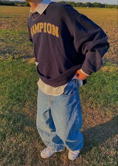 a boy standing in the grass with his hands on his hips wearing a champion sweatshirt