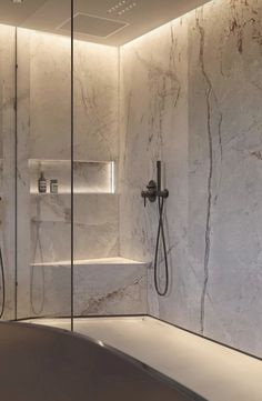 a bathroom with marble walls and flooring, shower head, and bathtub in the corner