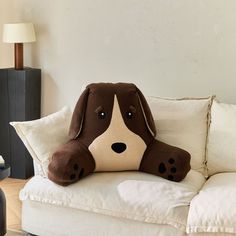 a brown and white dog pillow sitting on top of a couch next to a lamp