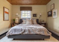 a bed sitting in a bedroom under a window next to a wooden ceiling with pictures on the wall