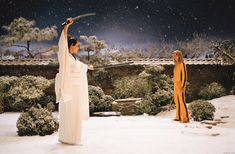 two women dressed in ancient chinese clothing holding swords and pointing them to the sky with snow falling on them