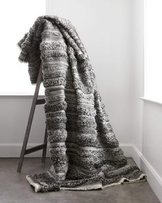 a blanket sitting on top of a wooden chair next to a white wall and window