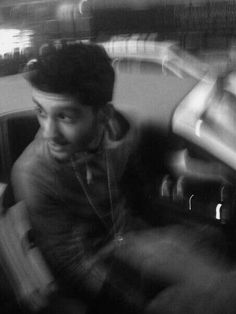 a black and white photo of a man sitting in a car talking on the phone