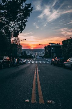 cars are parked on the street as the sun is setting in the distance behind them